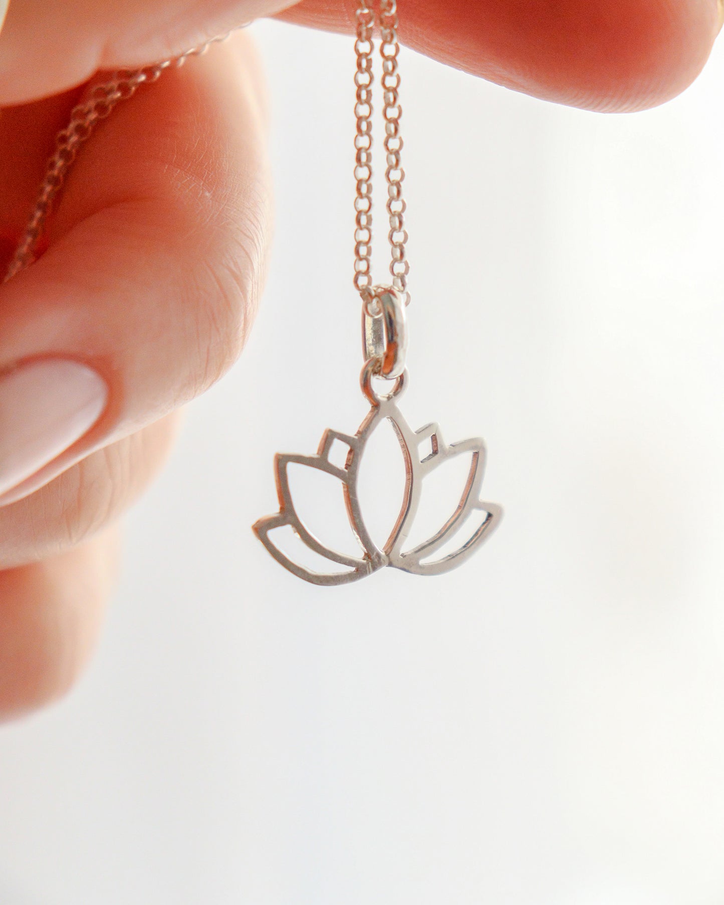Una mano sostiene un collar con un colgante de plata calado en forma de flor de loto, colgado de una fina cadena de plata.