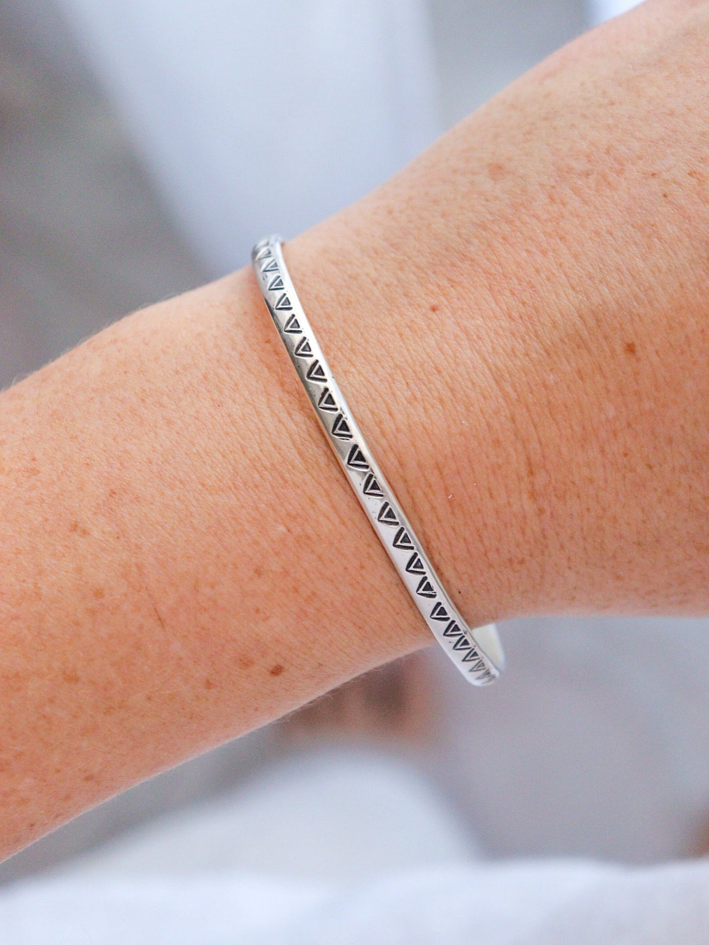 Pulsera TRILO de plata de ley con un diseño tribal y artesanal, mostrada en la muñeca. La pieza central es una obsidiana plateada de forma irregular, y el brazalete está decorado con un patrón de triángulos estampados.