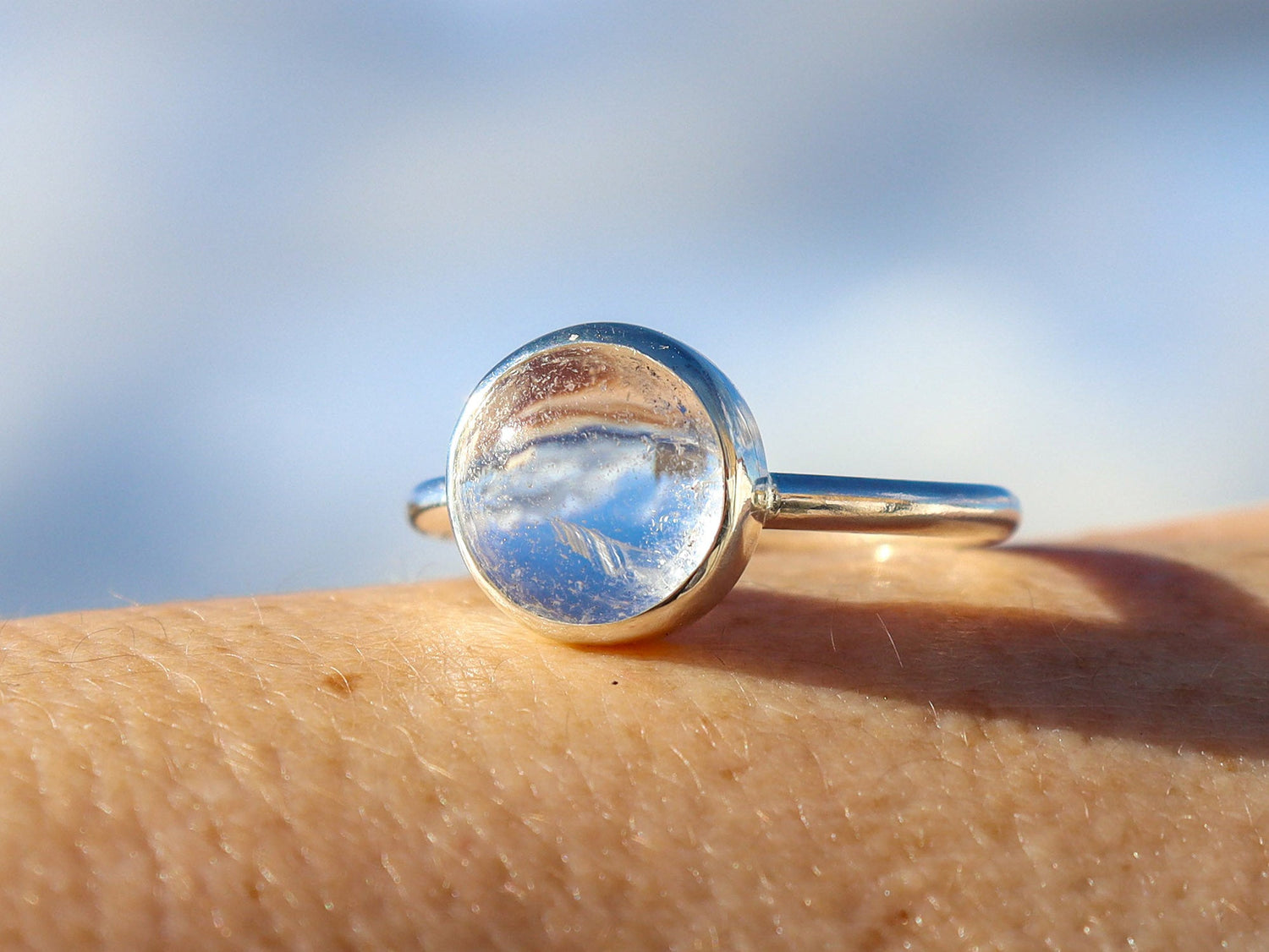 Anillo Diáfano, con cuarzo cristal de forma redonda engastado en plata de ley. Apoyado sobre la piel de una persona.