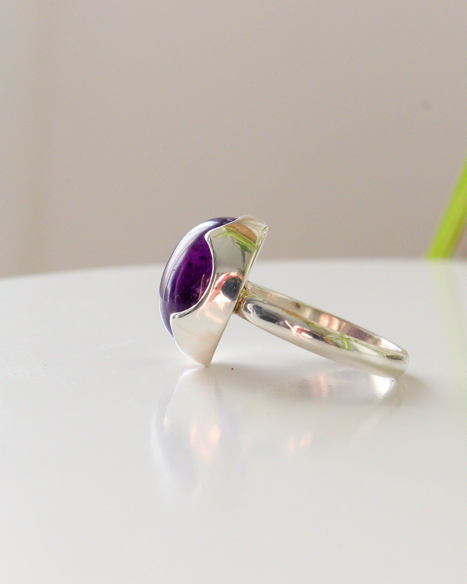 Perfil de anillo de plata de ley con Amatista ovalada, engastada sobre bisel con forma de onda Sobre fondo claro.