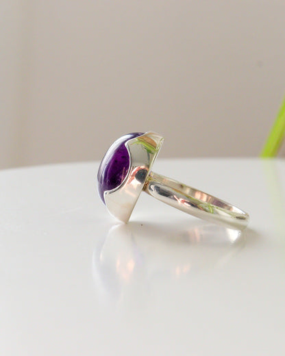 Perfil de anillo de plata de ley con Amatista ovalada, engastada sobre bisel con forma de onda Sobre fondo claro.