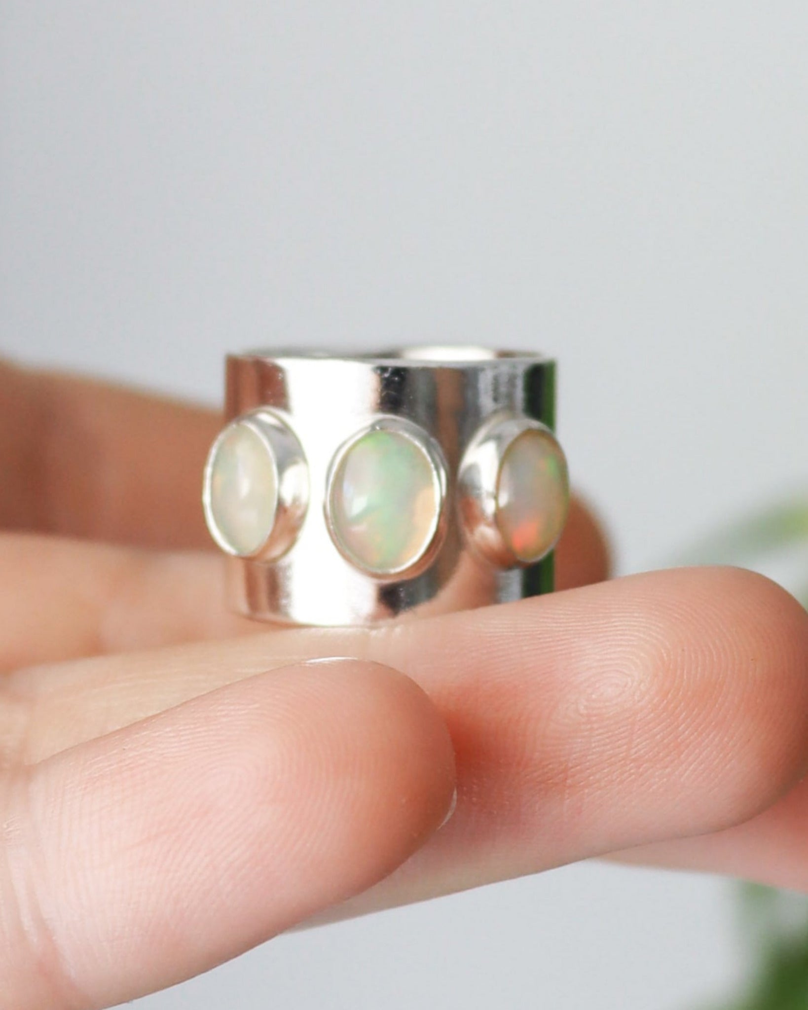 Primer plano del anillo ancho de plata de ley con 3 ópalos etiopes, sostenido en una mano.
