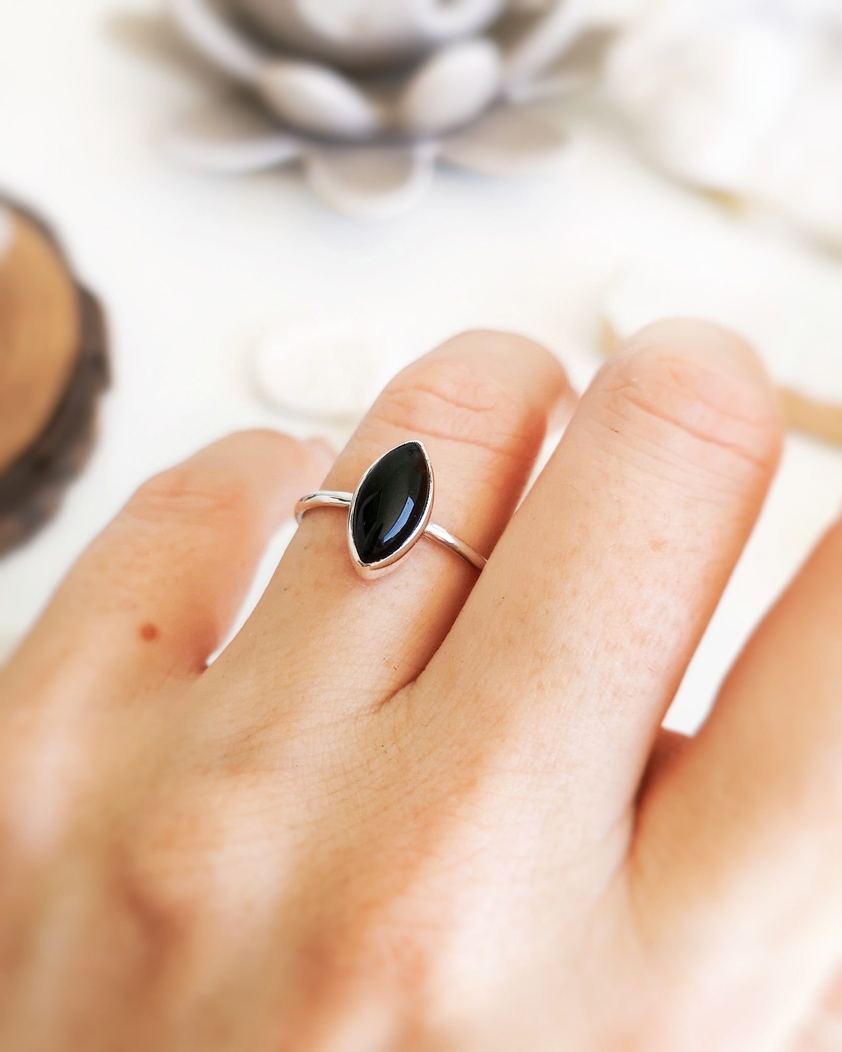 Anillo Esencial Mirar de plata con una piedra negra de forma marquise en el centro, llevado en el dedo anular de una mano.