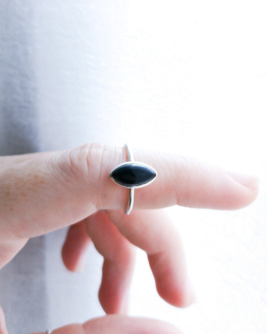 Anillo Esencial Mirar de plata con una piedra negra de forma marquise en el centro, llevado en el dedo índice de una mano.