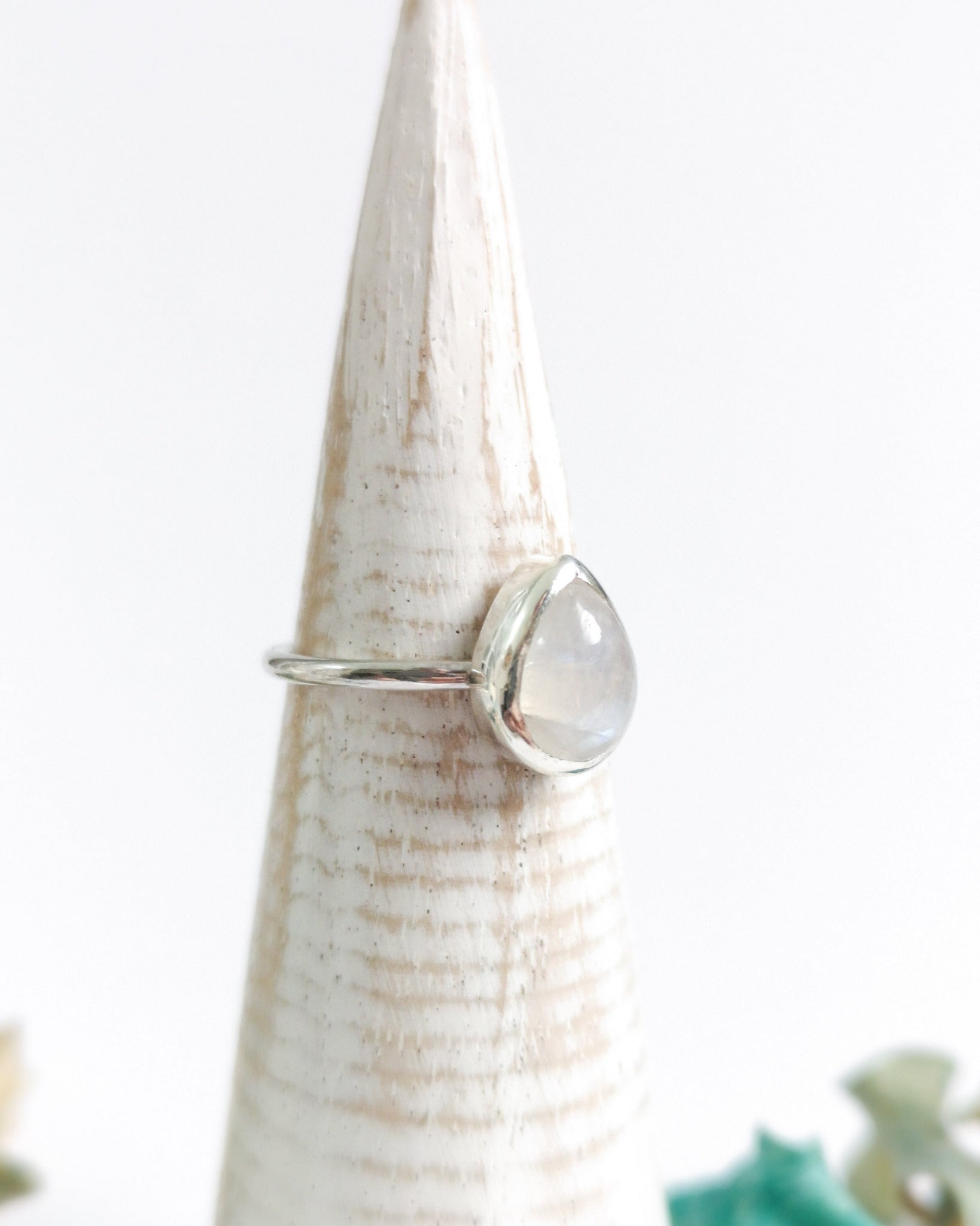 El anillo ESENCIAL de plata con una piedra lunar ovalada y translúcida, engarzada en un bisel simple, descansa sobre un expositor de anillo cónico de madera clara.
