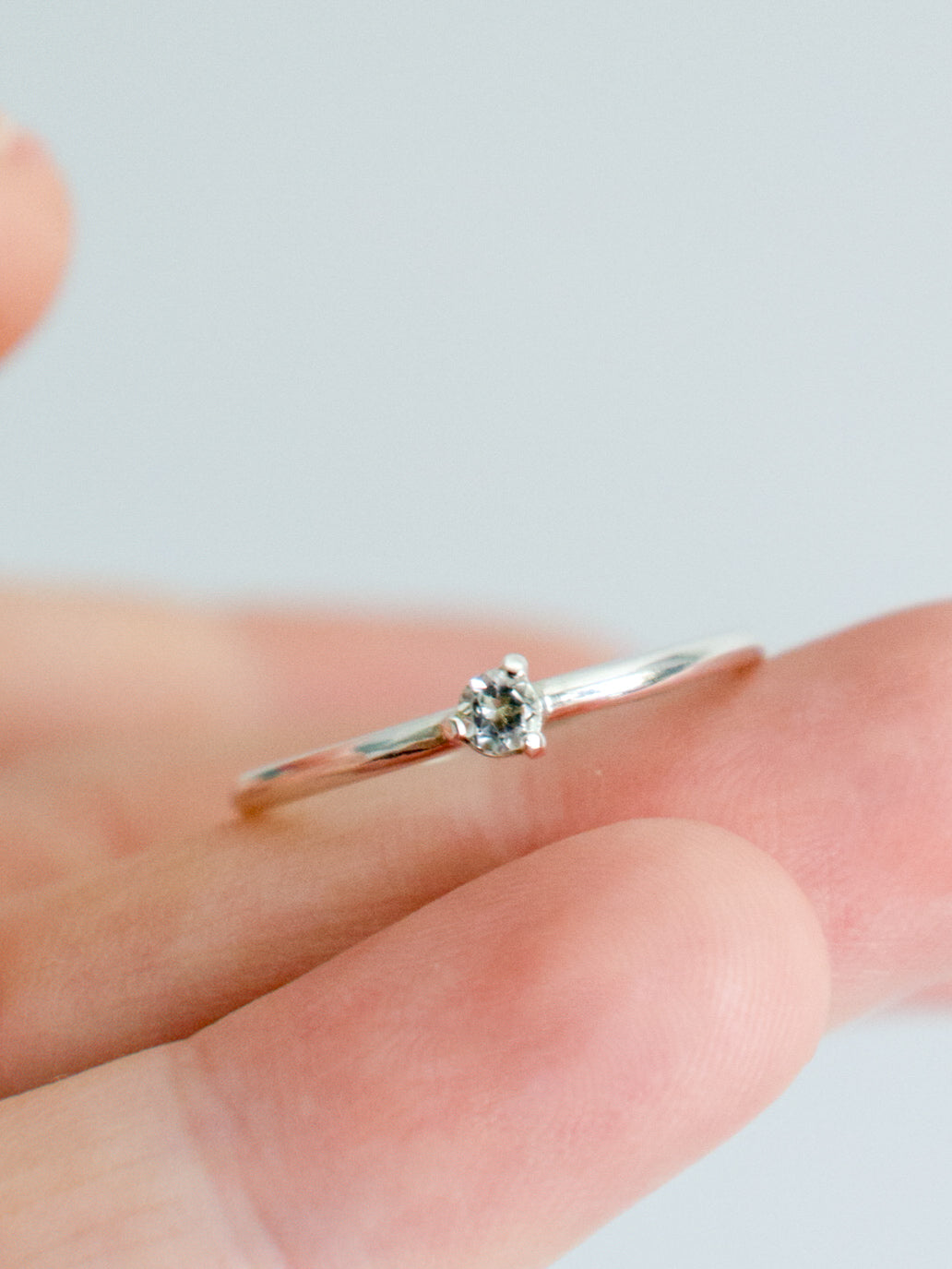 Anillo solitario de plata de ley (plata 925) con topacio blanco talla brillante sobre dedo. Banda fina y pulida, engaste de tres garras. Joyería fina.