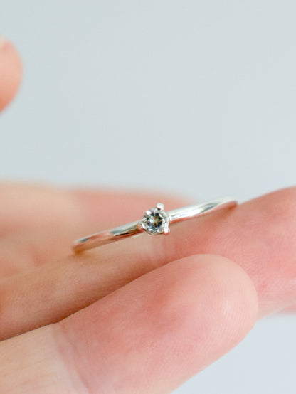 Anillo solitario de plata de ley (plata 925) con topacio blanco talla brillante sobre dedo. Banda fina y pulida, engaste de tres garras. Joyería fina.