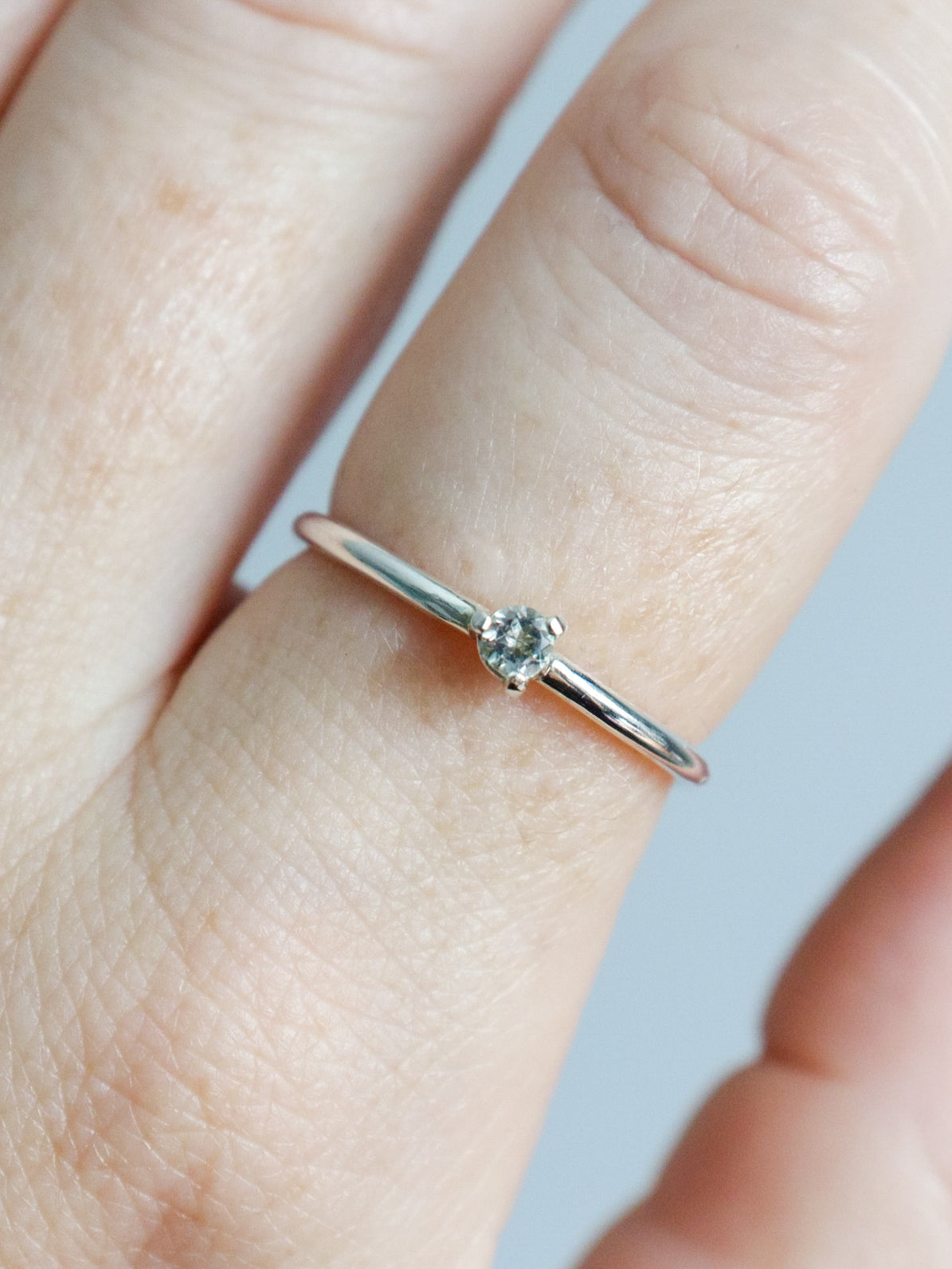 Anillo solitario de plata de ley (plata 925) con topacio blanco talla brillante. Vista en primer plano del anillo puesto en el dedo destacando la brillantez de la piedra redonda y el engaste de tres garras. Diseño fino, elegante y clásico de joyería fina.