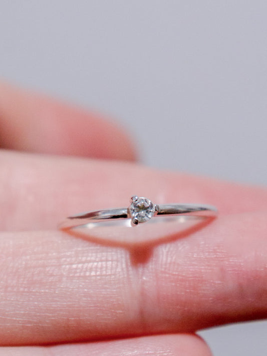 Anillo solitario de plata de ley (plata 925) con topacio blanco talla brillante sobre dedo. Banda fina y pulida, engaste de tres garras. Joyería fina.