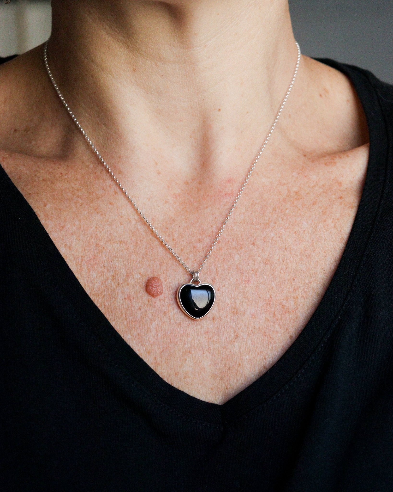 Una persona lleva puesto un collar con un colgante de ónix negro en forma de corazón, engarzado en plata, sobre una camiseta oscura.
