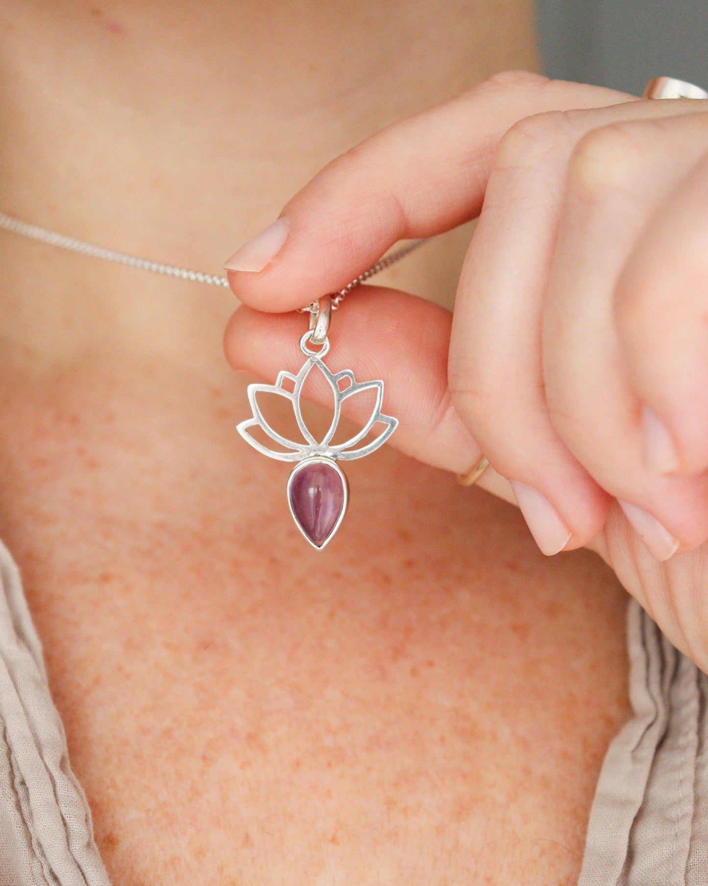 Una persona lleva puesto un collar de plata con diseño de flor de loto y una amatista en forma de lágrima, sobre una camiseta clara.