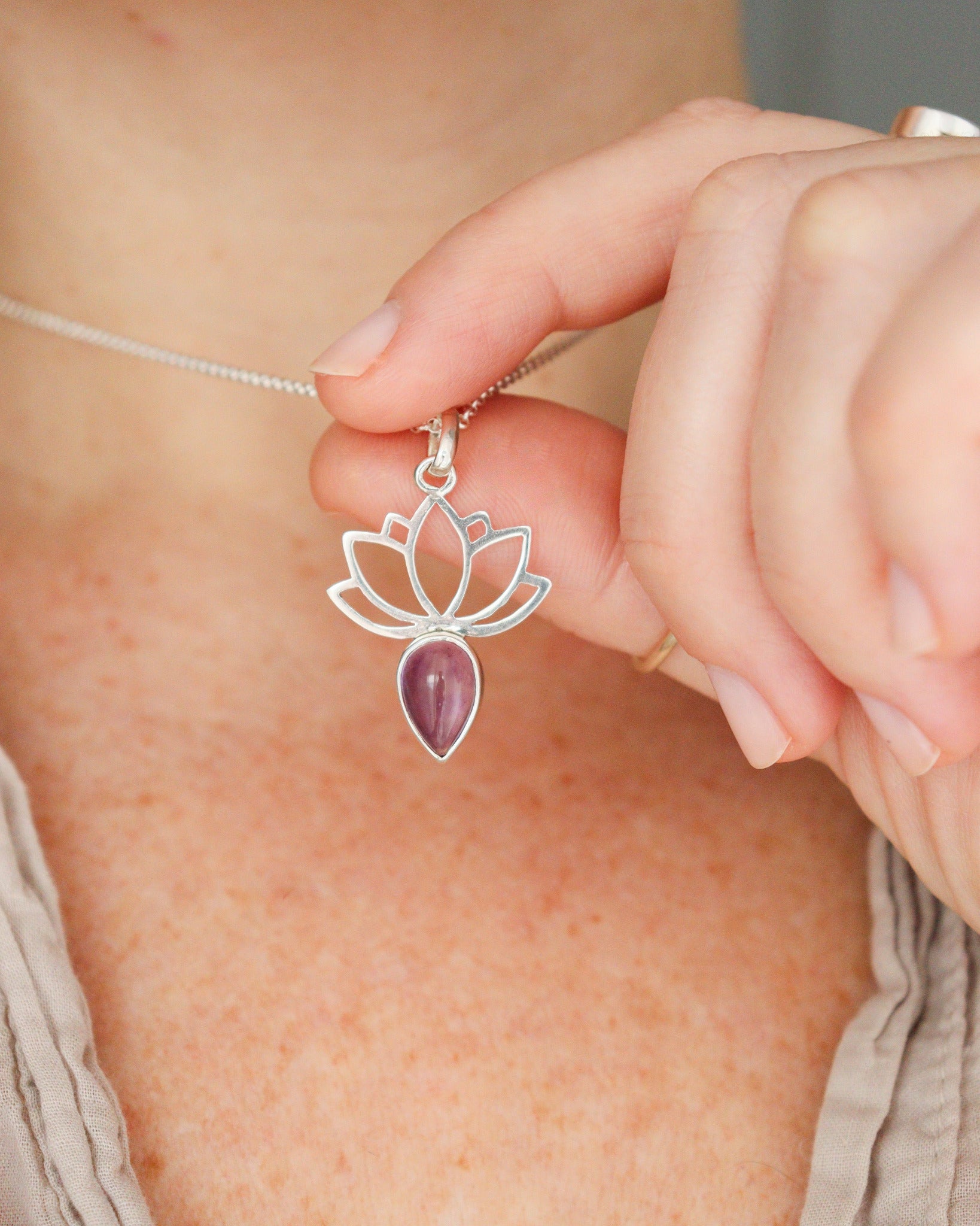 Una persona lleva puesto un collar de plata con diseño de flor de loto y una amatista en forma de lágrima, sobre una camiseta clara.