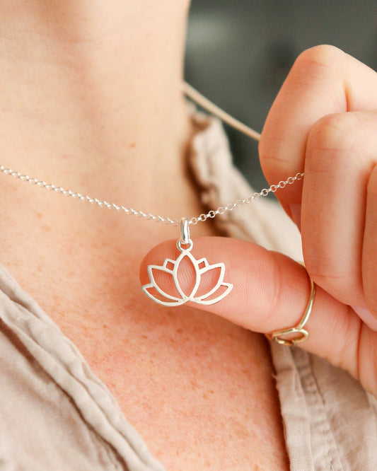 Una persona con un anillo sostiene un collar con un colgante de plata calado en forma de flor de loto, mostrándolo de cerca.