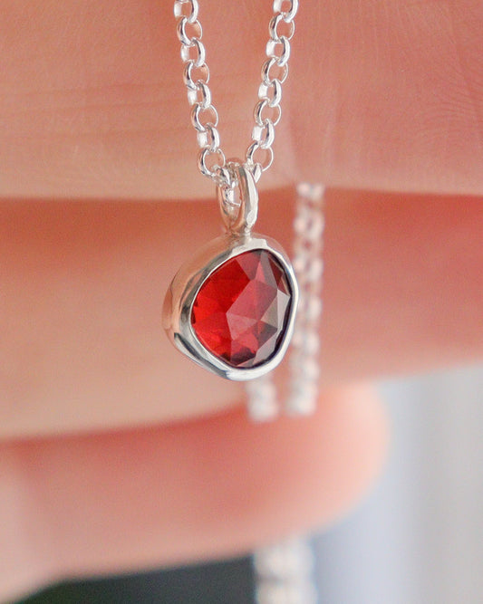 Mano sostiene el colgante de mini granate ojo de talla rosa con su cadena de plata.