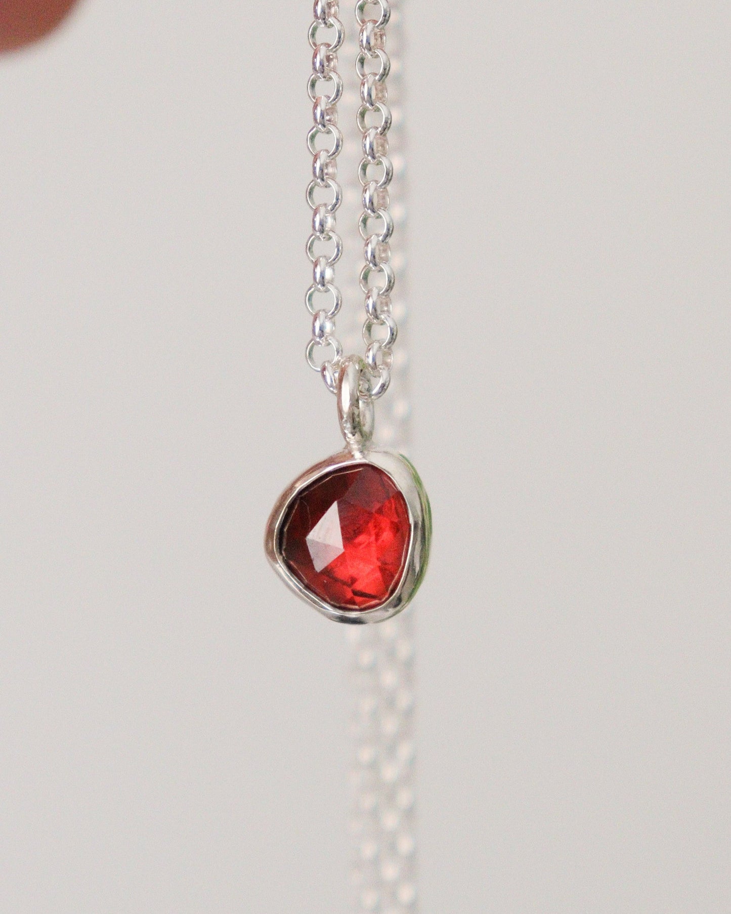 Colgante con mini granate rojo de talla rosa, colgando de su cadena de plata, sobre fondo blanco.