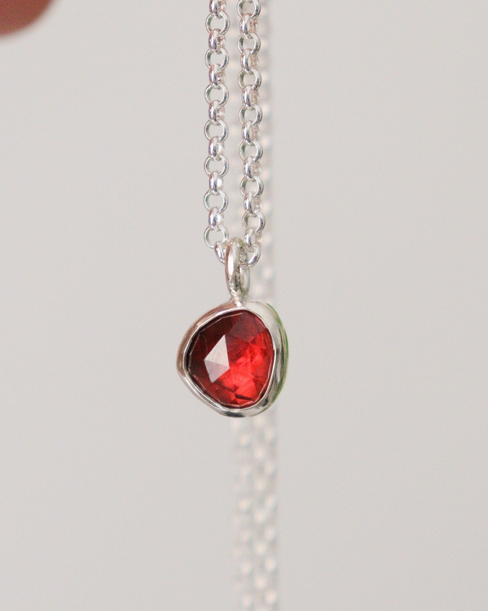 Colgante con mini granate rojo de talla rosa, colgando de su cadena de plata, sobre fondo blanco.