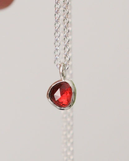 Colgante con mini granate rojo de talla rosa, colgando de su cadena de plata, sobre fondo blanco.