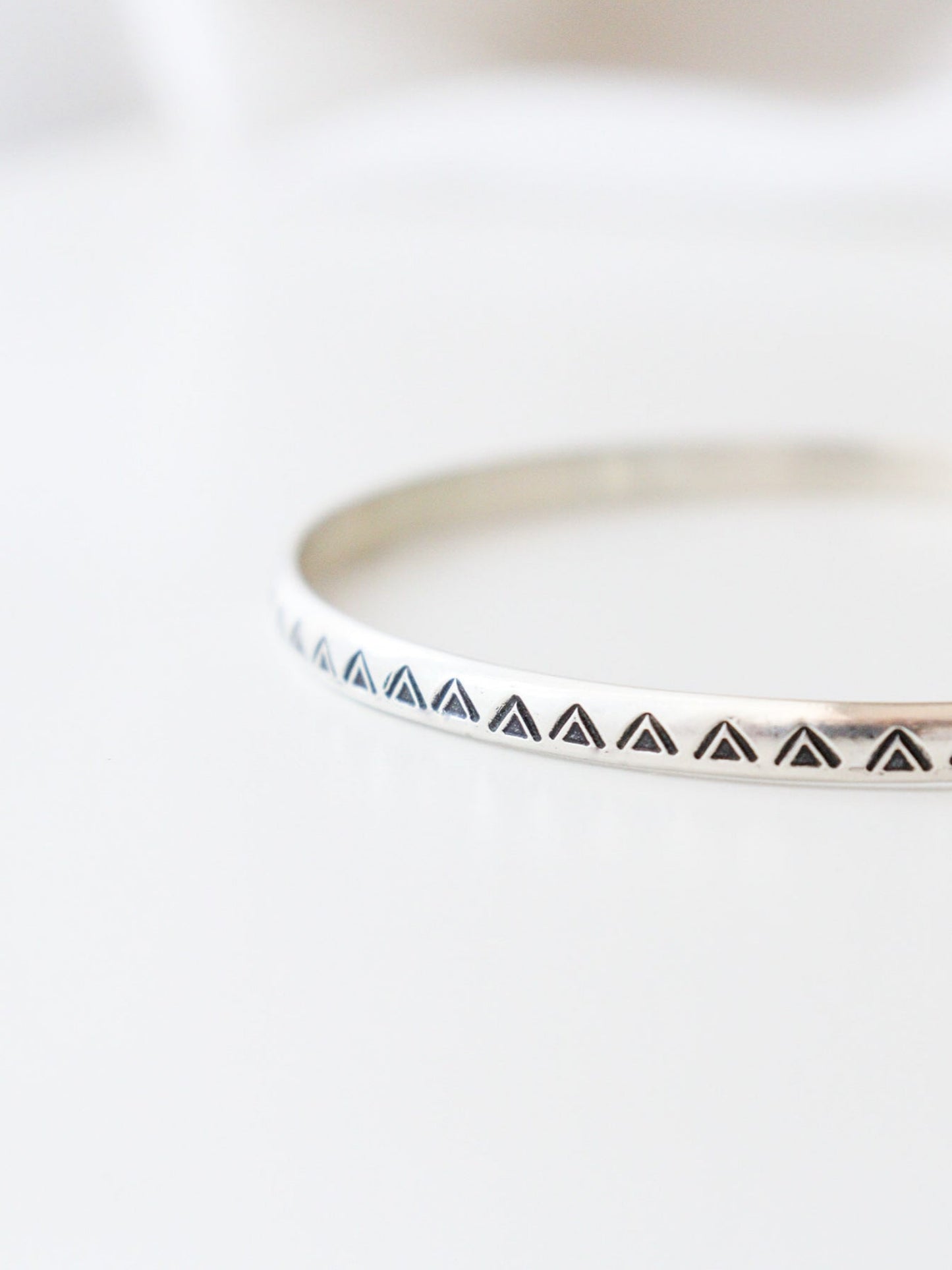 Vista frontal en detalle de la pulsera TRILOde plata de ley, con un diseño minimalista y geométrico. El brazalete  tiene un patrón de triángulos estampados, y está fotografiado con un fondo claro.