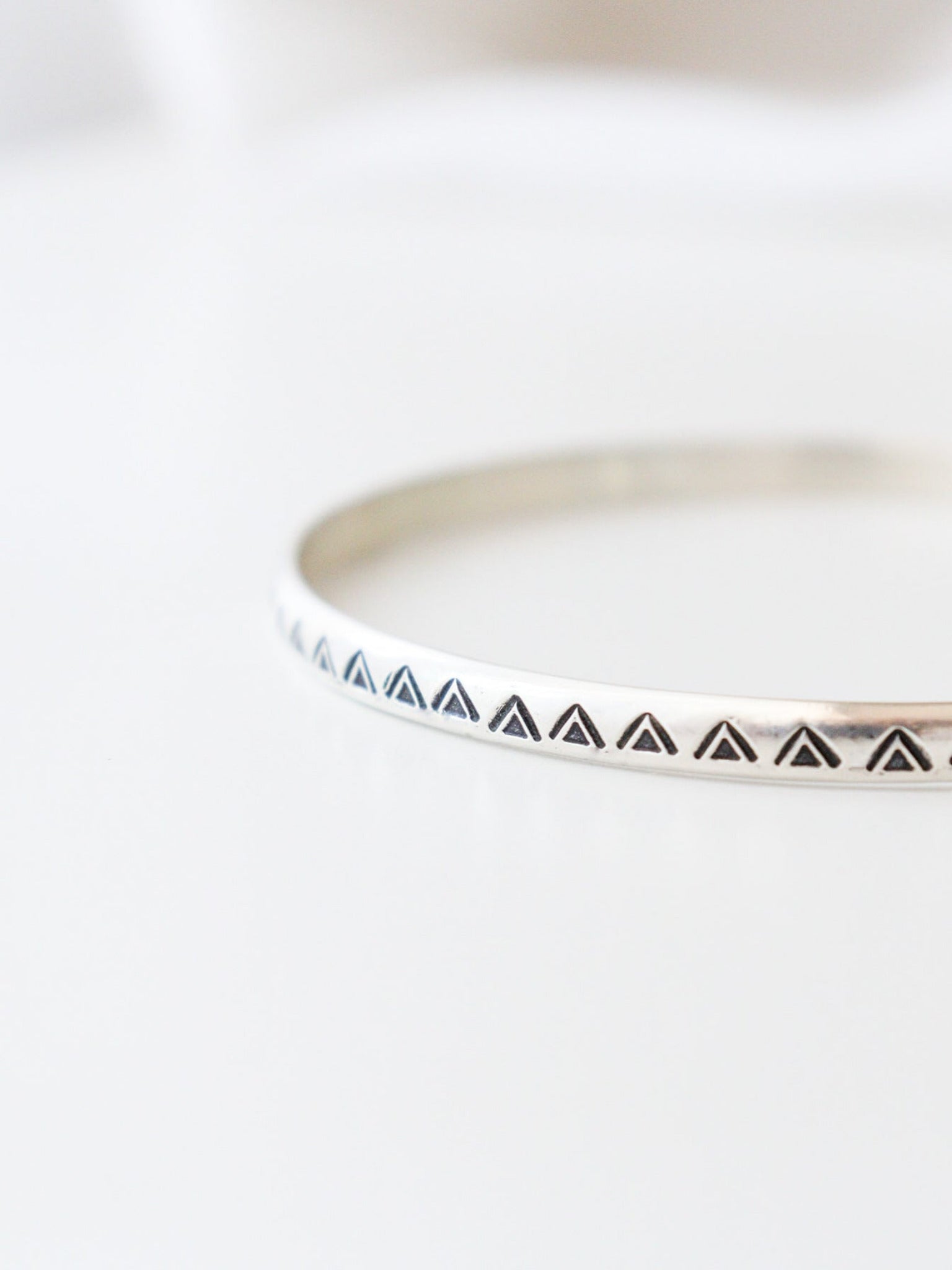 Vista frontal en detalle de la pulsera TRILOde plata de ley, con un diseño minimalista y geométrico. El brazalete  tiene un patrón de triángulos estampados, y está fotografiado con un fondo claro.