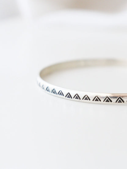 Vista frontal en detalle de la pulsera TRILOde plata de ley, con un diseño minimalista y geométrico. El brazalete  tiene un patrón de triángulos estampados, y está fotografiado con un fondo claro.