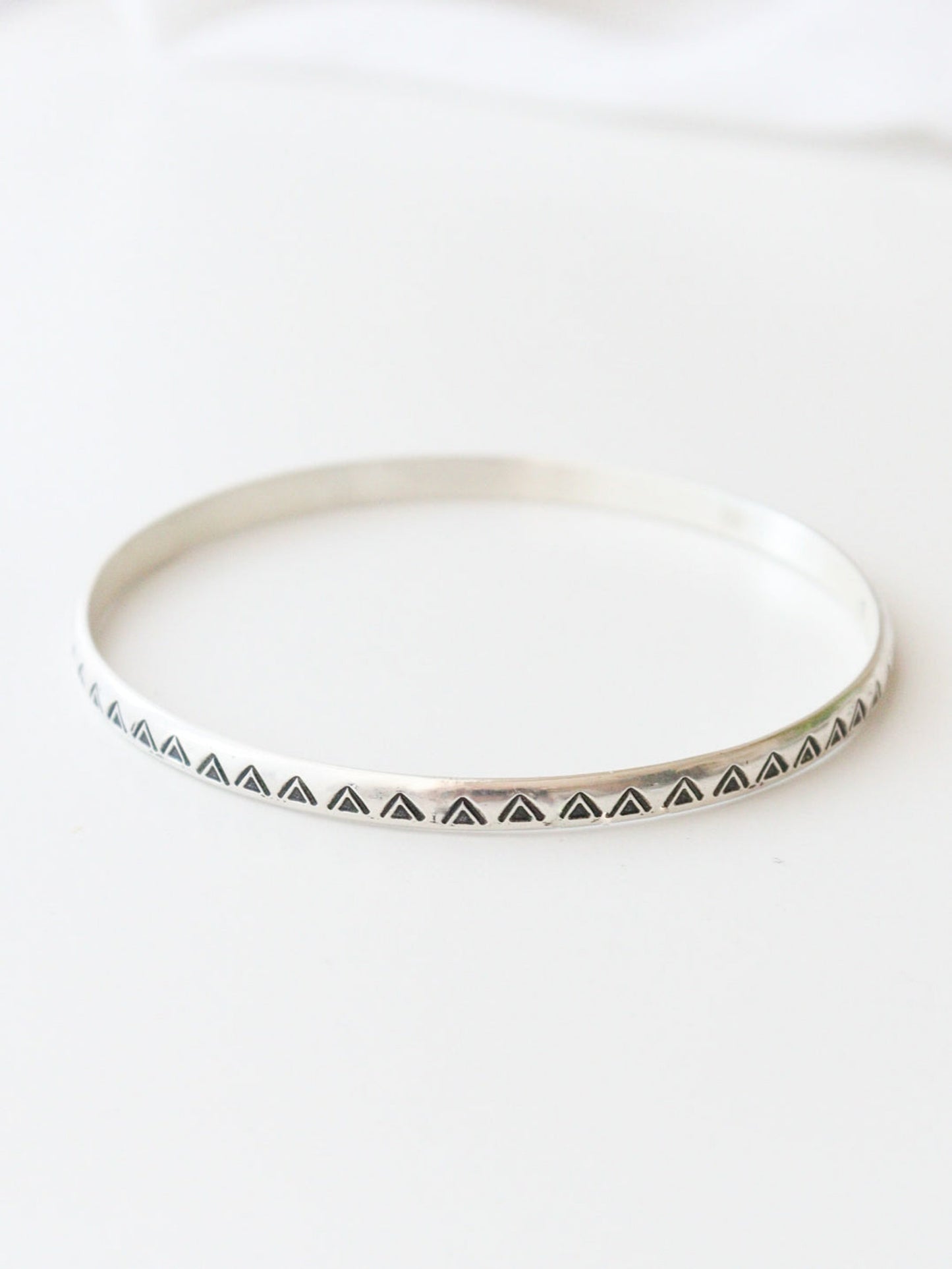 Primer plano de la pulsera TRILO de plata de ley con un diseño tribal y bohemio. El patrón de triángulos grabados decora el metal, sobre un fondo claro.