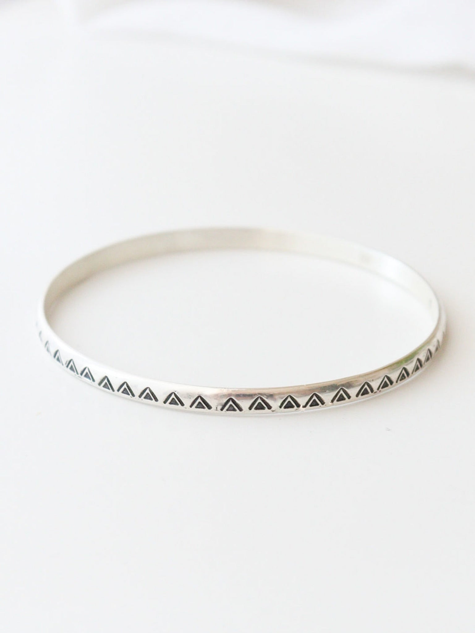 Primer plano de la pulsera TRILO de plata de ley con un diseño tribal y bohemio. El patrón de triángulos grabados decora el metal, sobre un fondo claro.