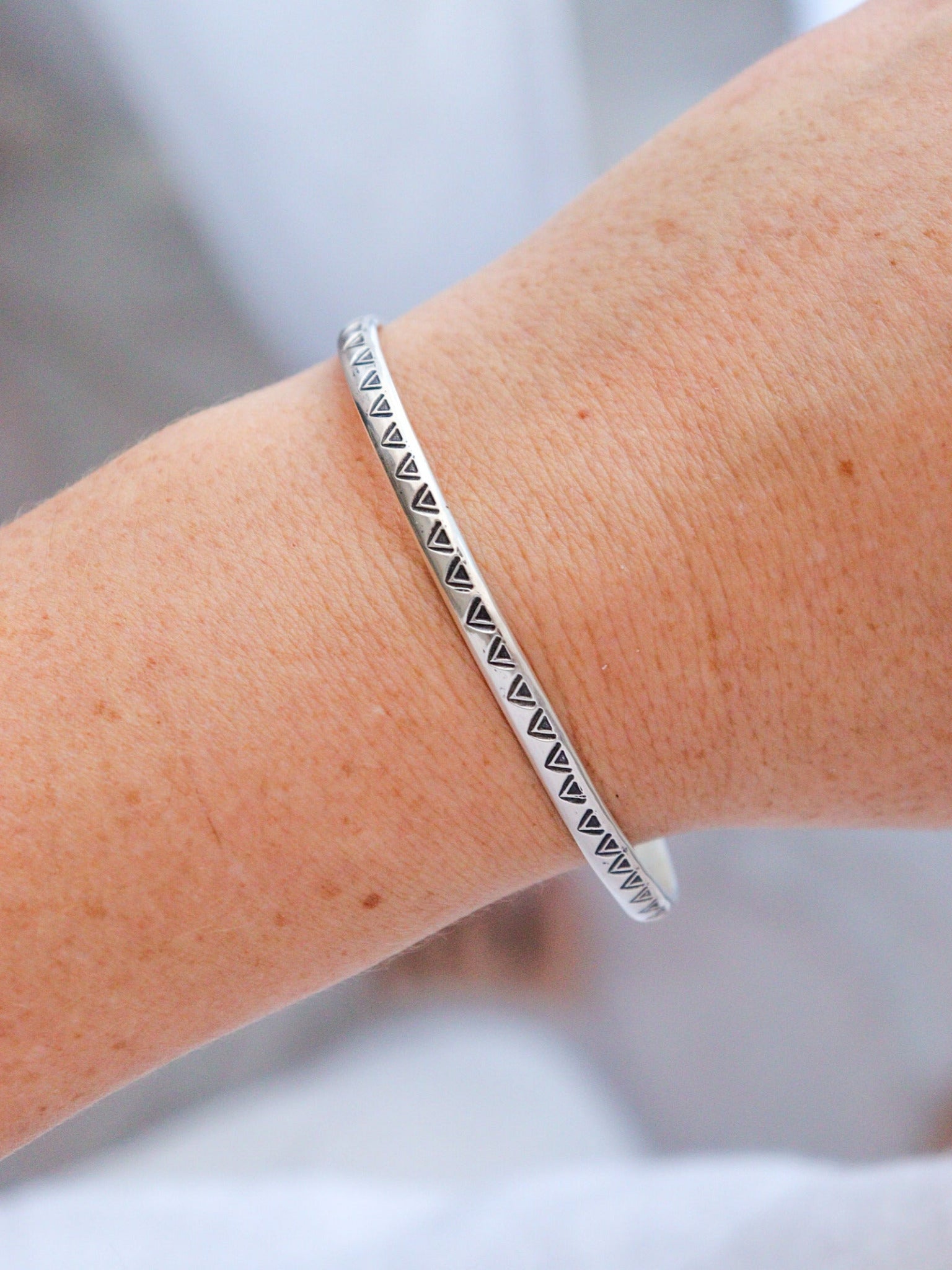 Pulsera TRILO de plata de ley con un diseño tribal y artesanal, mostrada en la muñeca. La pieza central es una obsidiana plateada de forma irregular, y el brazalete está decorado con un patrón de triángulos estampados.