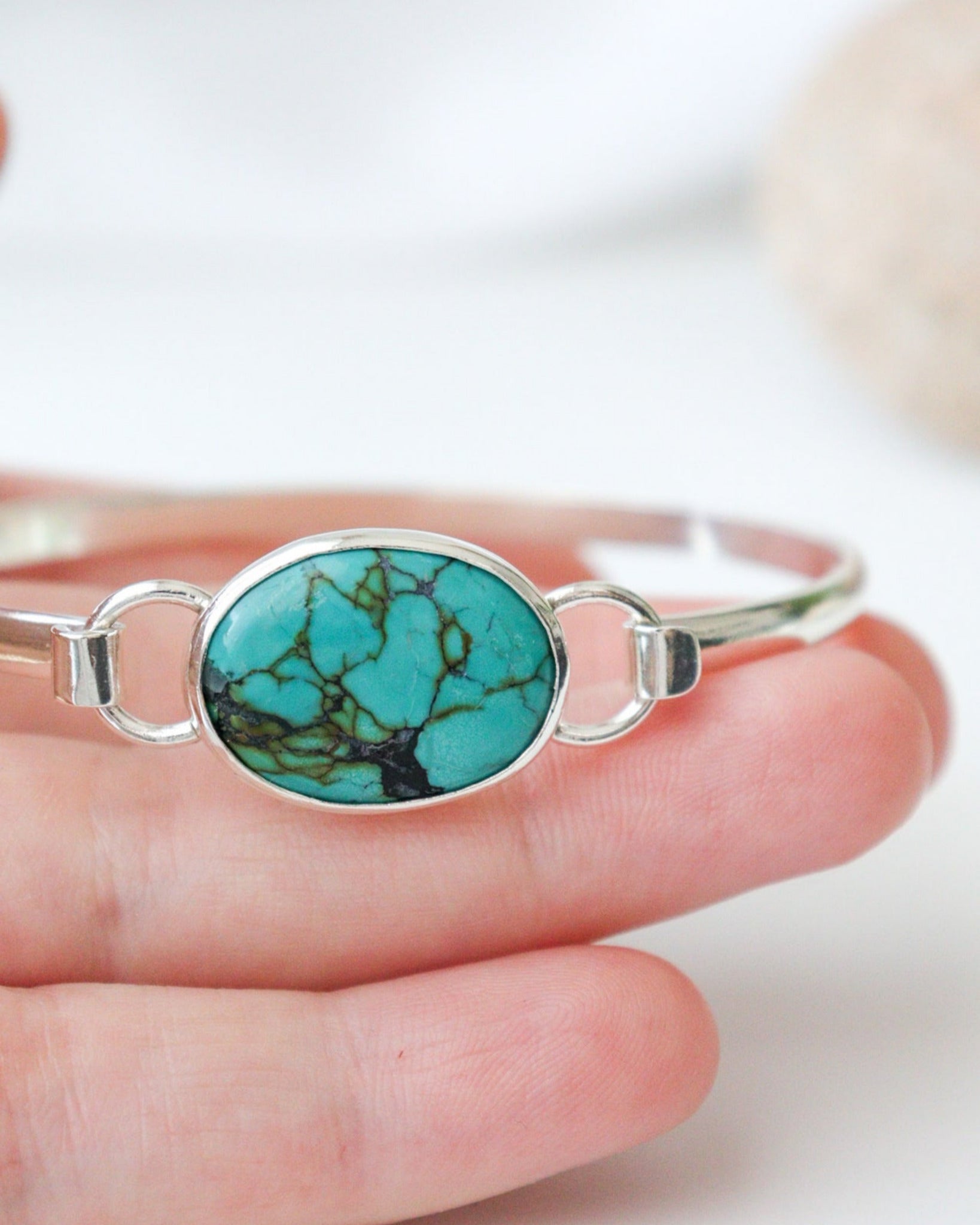 Primer plano de mano que sostiene la pulsera EUNOIA con turquesa tibetana de forma ovalada y estructura de plata de ley.