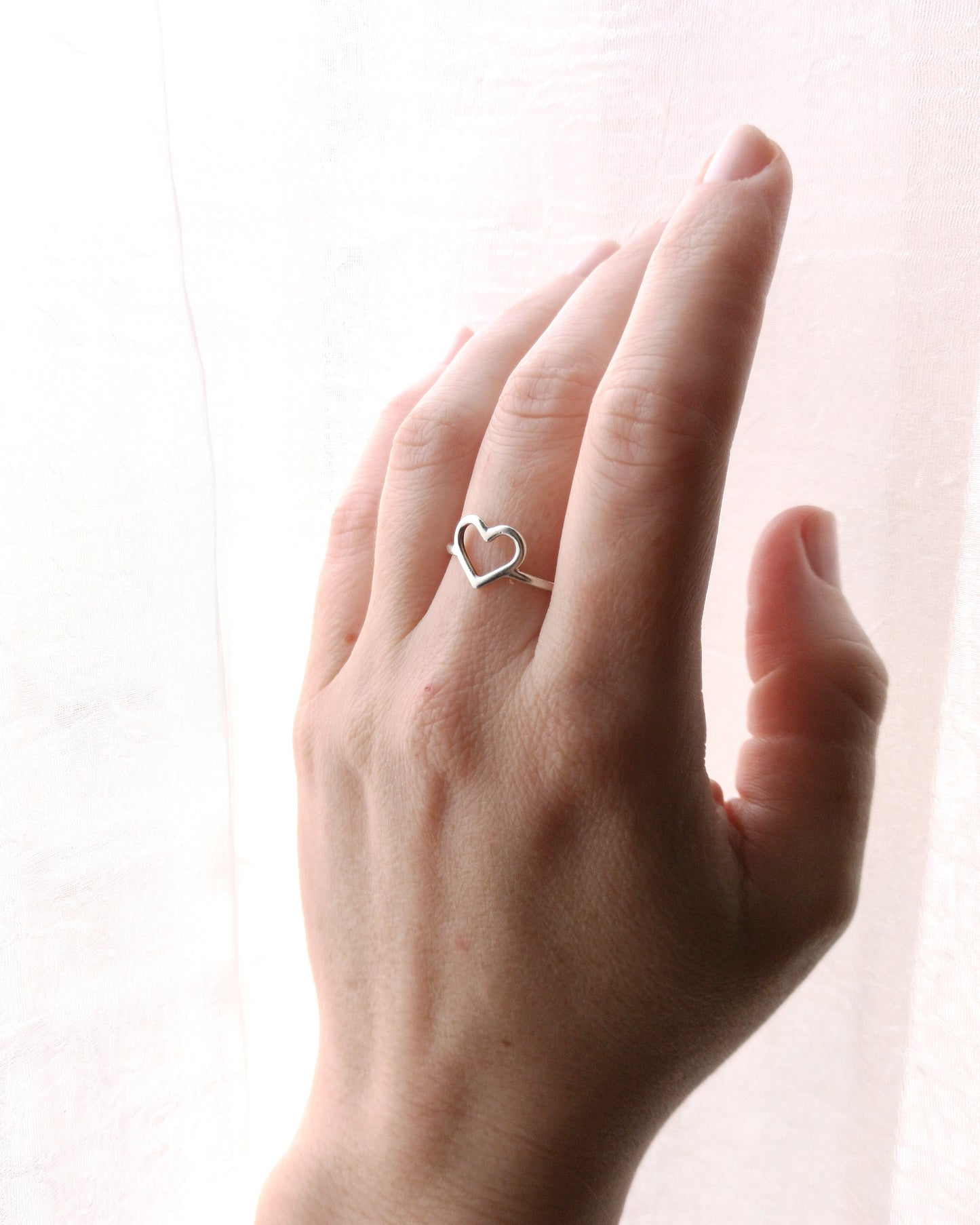 Imagen en primer plano de mano en medio perfil con anillo CORAZÓN en dedo medio. Fondo blanco.